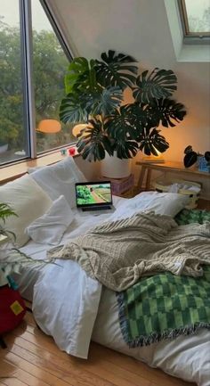 a bed with a laptop on top of it next to a large potted plant