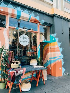 a colorful shop front with an assortment of handmade items on the table and behind it is a surfboard