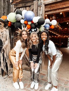 three women posing for a photo in front of a wooden door with balloons on it