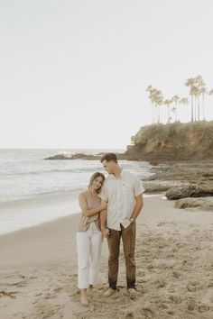 a man and woman standing on top of a sandy beach next to the ocean with palm trees