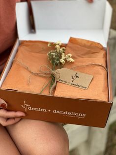 a person holding a box with flowers in it and a tag on the side that says denim + dandelions