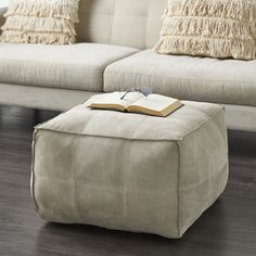 a book sitting on top of a foot stool in front of a couch with pillows