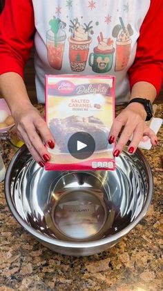 a woman in red shirt holding up a bowl with cake mix inside it on top of a counter