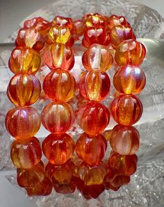 a bunch of orange glass beads sitting on top of a clear plate with a silver spoon in the background