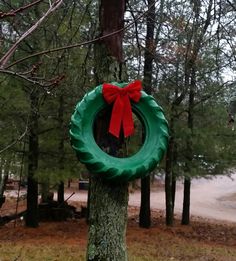 a green wreath with a red bow hanging from it's side in the woods