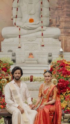 a man and woman sitting next to each other in front of a statue with flowers