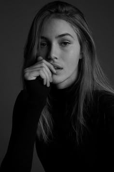 a black and white photo of a woman with her hand on her chin looking at the camera