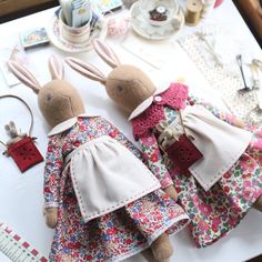 two stuffed rabbits dressed in clothes sitting on top of a table