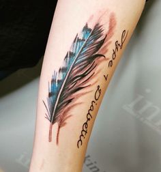 a woman's arm with a blue and black feather tattoo on it that says, she is beautiful