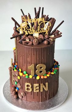 a birthday cake with chocolate frosting and candies on the top is decorated in gold lettering