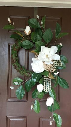 a wreath with white flowers and green leaves hangs on the front door's brown door