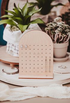 a wooden jewelry holder sitting on top of a table next to a potted plant