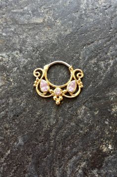 an ornate gold ring with pink stones on top of a stone slabd surface in the shape of a flower