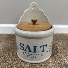 a salt can with a wooden lid on carpeted floor next to wall and door