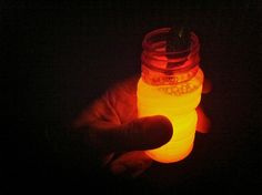 a hand holding a mason jar in the dark with glowing lights on it's lid