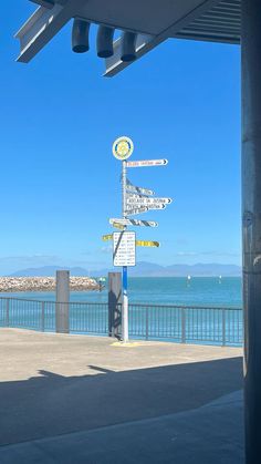 there are many signs on the post by the water's edge that point in different directions