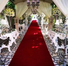 a red carpeted aisle with white chairs and chandeliers on either side is decorated with flowers