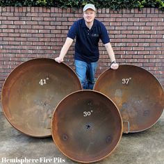 a man standing in front of three large metal pans with numbers on them next to a brick wall