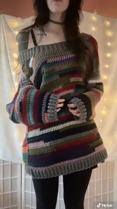 a woman wearing a multicolored sweater and black tights stands in front of a white curtain