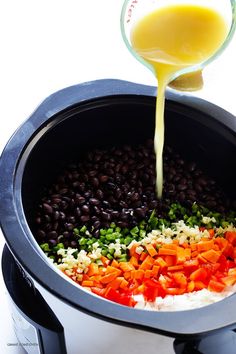 a person pouring orange juice into a slow cooker filled with vegetables and black beans