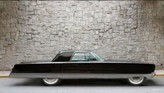 an old black car parked in front of a stone wall