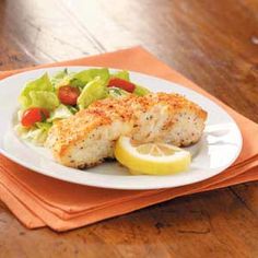 a white plate topped with fish next to a salad and lemon wedges on top of an orange napkin