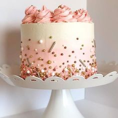 a white cake with pink frosting and gold sprinkles on a stand