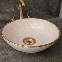 a white and gold bathroom sink sitting on top of a marble counter next to a faucet