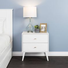 a bedroom with blue walls, white furniture and a lamp on the nightstand next to the bed