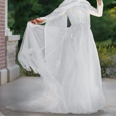 a woman in a white wedding dress is holding an umbrella and wearing a long veil