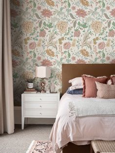 a bedroom with floral wallpaper and bedding in the foreground is a dresser