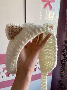 a hand holding up a knitted hat with a cat ears on it's side