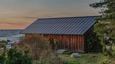 a small wooden building sitting on top of a lush green field next to the ocean