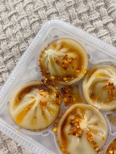 four dumplings in a plastic container with sauce and seasoning on them sitting on a table