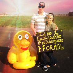 a man standing next to a woman holding a sign that says i'd be lucky duckie if you're my date