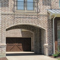 a brick house with an arched doorway and two garage doors on either side of it