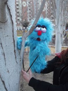 a woman holding an umbrella next to a tree with a blue furry animal on it