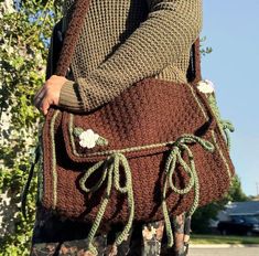 a woman carrying a crocheted purse with flowers on the handles and straps, in front of a tree