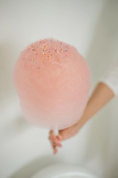 a person holding a large pink ball of cotton candy in their right hand and the other hand is pointing at it