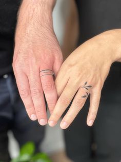 two people holding hands with tattoos on their fingers and the other hand has a ring