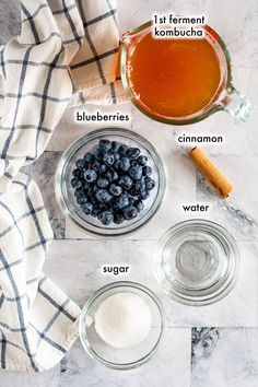 ingredients to make blueberry muffins laid out on a marble counter top, including sugar, cinnamon and syrup