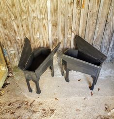 two metal planters sitting next to each other on the ground in front of a wooden wall