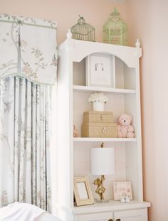 a white book shelf sitting next to a bed in a child's room with pink walls