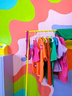 colorful clothing hanging on clothes rack in children's room with multicolored wall