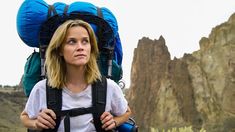 a woman with a backpack on her back standing in front of some rocks and mountains