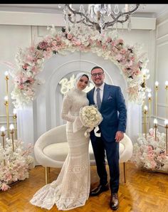 a man and woman posing for a photo in front of a floral arch with chandelier