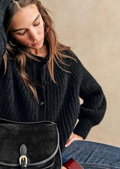 a woman sitting on the floor with her handbag in front of her face and looking down