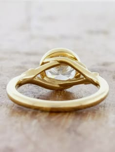 a yellow gold ring with a diamond on the top, sitting on a wooden surface