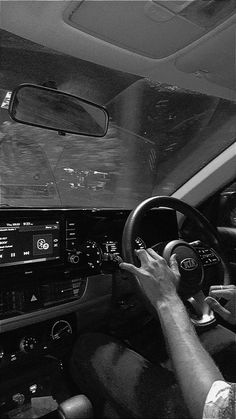 black and white photograph of man driving car with steering wheel in foreground, dashboard lights on