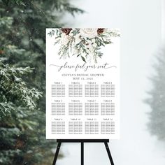 a white sign with flowers and greenery on it in front of snow covered trees